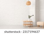 Wooden coffee table with eucalyptus branches in vase, folding screen and pouf near white brick wall