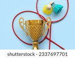 Gold cup with badminton rackets and shuttlecocks on blue background