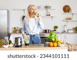 Mature woman drinking healthy smoothie in kitchen