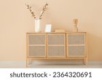 Vase with cotton branches, decor and blank frame on wooden sideboard near beige wall