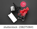 Composition with shopping carts, gadgets and gift box on black background. Cyber Monday sale