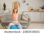Young sporty woman training with fitness ball at home