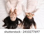 Asian mother with her little daughter relaxing on bed, top view