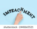 Small photo of Female hand with black letters spelling word IMPEACHMENT on blue background