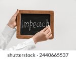 Small photo of Woman writing word IMPEACH on chalkboard against white background