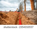 Small photo of Network cables in red corrugated pipe are buried underground on the street. underground electric cable infrastructure installation.