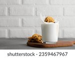 glass of milk with splash and chocolate chip cookies on wooden stand with white brick wall as background