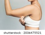 Close-up of a young caucasian blonde woman grabbing skin on her upper arm with excess fat isolated on a gray background. Pinching the loose and saggy muscles. Overweight concept