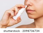 Cropped shot of a young caucasian woman using nasal spray for a runny nose and congestion isolated on a white background. Treatment of the disease. Rhinitis, sinusitis, cold. Dependence on drops