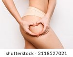 Small photo of Cropped shot of a young woman demonstrating white stretch marks from a sharp weight loss or weight gain with hands forming the heart on her thigh isolated on a white background. Changes of the body