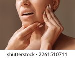 Small photo of Cropped shot of young woman suffering from jaw pain holding her chin with hands on brown background. Inflammation of cervical lymph nodes, Diseases of ENT organs, facial, trigeminal nerve, toothache