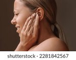 Profile of a young caucasian blonde woman holding her ears with her hands isolated on a dark brown background. Pain and tinnitus, ear otitis