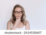 Small photo of A young caucasian thoughtful blonde woman with wavy hair in glasses imagining, thinking looking up at empty copy space for ads, promo, offer, quote, text, slogan isolated on a light background