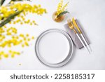 Festive table setting for the spring celebration of women's day, birthday or mother's day with yellow mimosa flowers on a light background with vase. Top view and copy space.