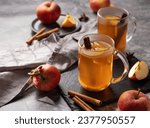 Homemade apple punch with fresh apples, cinnamon and spices in cups on dark background with fresh fruits. A hot, healthy autumn or winter drink. The concept of a homely cozy atmosphere.