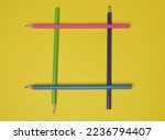 Small photo of Colored pencils are laid out in the form of a tic-tac-toe game on a yellow background.