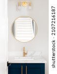 Small photo of A bathroom with a blue vanity cabinet, marble countertop, and a gold faucet, light fixture, and circular mirror.