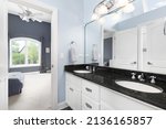 Small photo of OAK PARK, IL, USA - SEPTEMBER 23, 2021: A Jack and Jill bathroom with a white double vanity cabinet, black countertop, and blue walls looking towards a bedroom.
