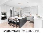 Small photo of CHICAGO, IL, USA - FEBRUARY 28, 2021: A luxurious kitchen with a large island, gold faucet and sputnik chandelier, stainless steel appliances, and white marble countertops.