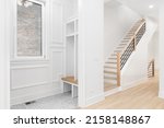 Small photo of An entryway with a bench, shelving, and tiled flooring looking towards a staircase with wood railing, hardwood floor, and wrought iron spindles.