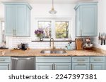 Small photo of A light blue kitchen detail with a granite countertop, gold faucet and light, and a white subway tile backsplash.