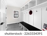 Small photo of A white mud room foyer with a dark grey tile floor, white shelving, coat hooks, and wood bench seat.