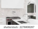 Small photo of A kitchen detail with a sink on an island's marble countertop with a stove, hood, and tiled backsplash in the background.