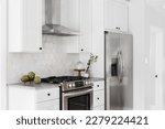 Small photo of A kitchen detail with white cabinets, stainless steel appliances, tan hexagon tile backsplash, and decorations on the grey marble countertop.