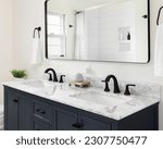 A beautiful bathroom with a dark blue vanity cabinet, marble countertop, and large mirror below a light.