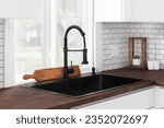 Small photo of A black kitchen sink and faucet detail in a white kitchen with a butcher block countertop, white subway tile backsplash, and cozy decor.