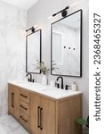 Small photo of A bathroom with marble and stacked vertical subway tiles, a white oak vanity cabinet, black framed square mirrors and faucets, and marble countertop.