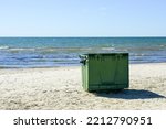a large green plastic garbage container on the seashore on a sandy beach