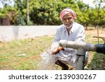 Happy Indian farmer after seeing water on borewell pipe at farmland - cocnept of happiness, poverty and water for agricultural works.