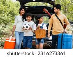 Happy indian fmaily with kids with picnic basket and travel lagguage at destination - concept safe car travel, transportation and vacation or holidays.