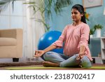 Indian peaceful pregnant woman in lotus pose doing meditation on yoga mat home - concept of relaxation, healthy pregnancy and self-care.