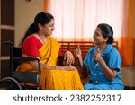 Small photo of Joyful Indian nurse building confidence or encouraging recovered sick woman on wheelchair at home - concept inspiration, assurance and rehabilitation