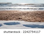 Cold sea with a pier and snow on the sandy shore. Black sea in winter.