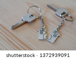 Pendant of key ring in shape of house divided in two parts on wooden background, closeup view. Dividing house when divorce, division of property and real estate.

