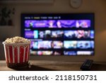 Close up of bowl of popcorn and remote control with tv works on  background. Evening cozy watching a movie or TV series at home. 