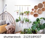 Small photo of Multiple macrame plant hangers with indoor houseplants and pot planters are hanging from a metal pole. Boho basket wall decor and wicker egg chair are use to add character to the cozy bohemian room.