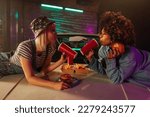 Small photo of Two young adult fashionable women are eating some takeout food on a hood of their car.
