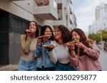 Four female multiethnic girlfriends eating slices of pizza and laughing on the streets