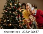 A shot of a Christmas tree being decorated with Christmas decoration by a little girl and her grandparents