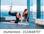 Small photo of Portrait of fitness athletic beauteous pregnant woman in uniform sportswear top, leggings. Doing yoga goasana exercise, meditating finding coordination, balance in sport center pink mat, bottle water