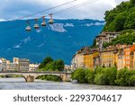 Isere river in Grenoble city skyline, Auvergne-Rhone-Alpes region, France. Pont Marius-Gontard bridge, Grenoble-Bastille Cable car (Telepherique) and Alps mountains on background