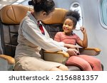 Small photo of Flight attendant help fasten the seatbelt for young little African American kid after boarding the airplane as a safety procedure before take off