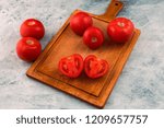 Small photo of Red tomatoes on a chopping Board, one tomato cut in two.