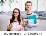Small photo of Young students near university with books, exercise books holding credit cards and smiling to camera. Modern college learners using cards for online banking, buying things online, receiving stipend