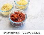 bacon bits, parmesan cheese and cheddar cheese in glass bowls on marble background