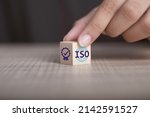 Small photo of ISO quality control certification concept. Hand flip ISO smart globe icons with check mark guarantee icon on wooden cube and copy space.